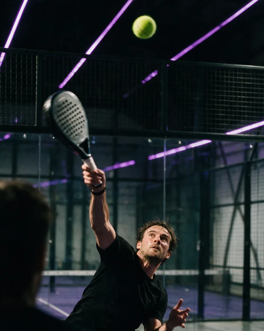 Spieler beim Smash, Ball in der Luft vor lila LED-Baendern